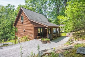 Un chalet rustique avec une allée en gravier, une terrasse en bois et des plantes en pot.