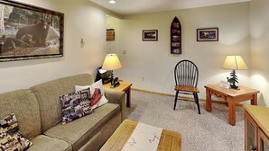A living room with a sofa, a coffee table, a wooden side table, a chair, and a lamp. There are framed pictures on the wall. - Hidden Treasure by Taylor Made Deep Creek (Oakland)