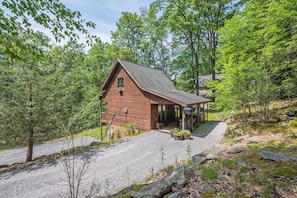 A wooden cabin with a gravel driveway and a covered porch.