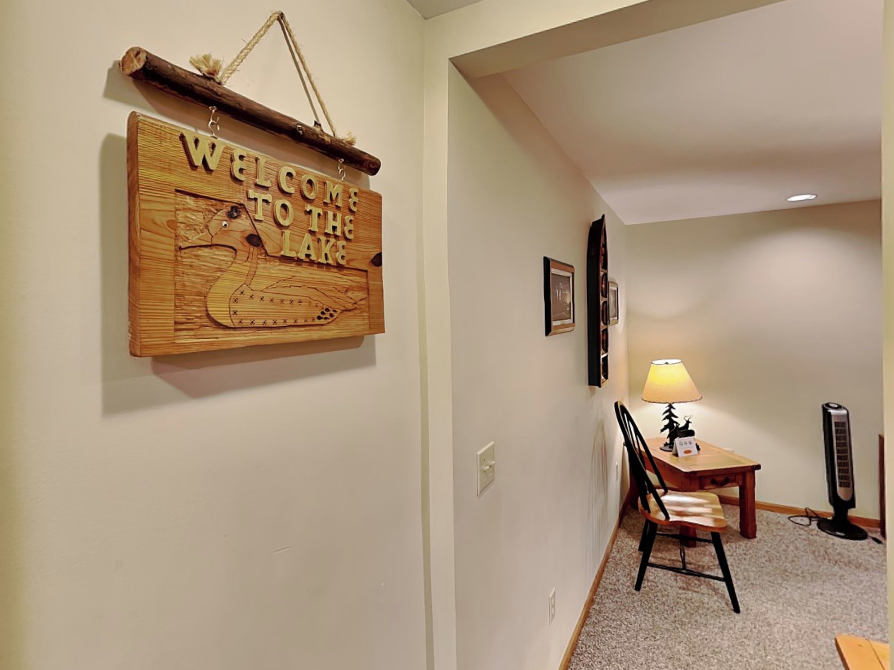 A hallway with a wooden welcome sign, a small table with a chair, a lamp, and a standing heater.