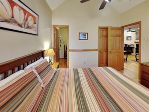 A bedroom with a striped bedspread, wooden headboard, and a ceiling fan.