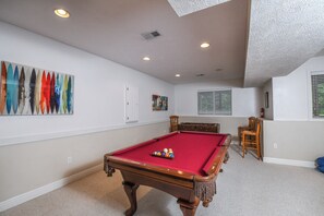A pool table with a red felt surface, surrounded by beige carpet. There are two wooden chairs and a small table with a red cloth. - Heavenly Grove by Taylor Made Deep Creek (Oakland)