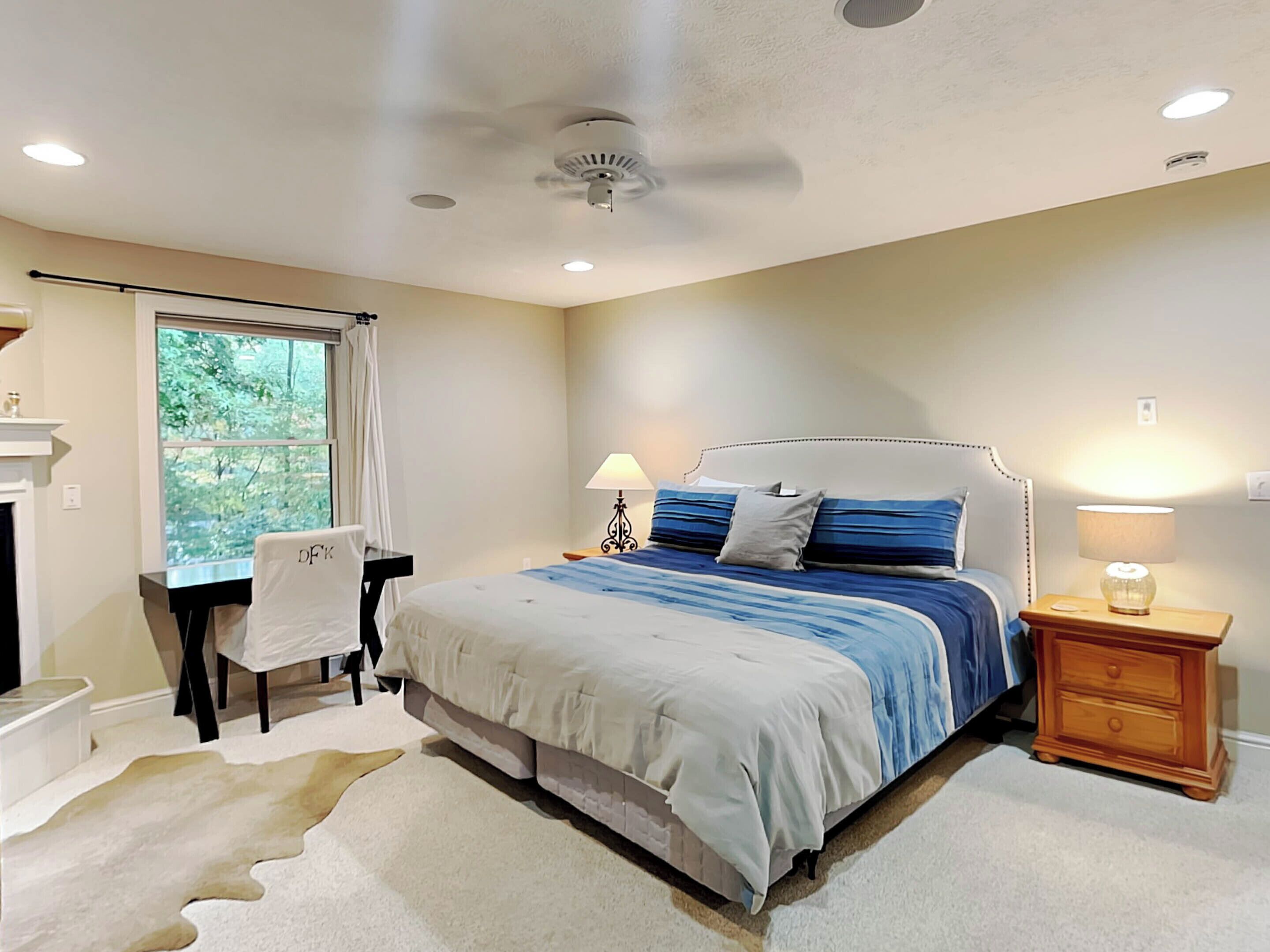 A bedroom with a bed, desk, chair, and a nightstand with a lamp.