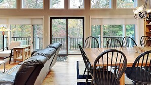 Una habitación amplia con techo alto, ventanas grandes, una zona de comedor con mesa y sillas de madera, un banco de cuero y un candelabro.