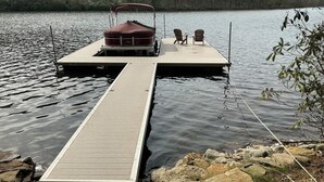 Un muelle de madera que se adentra en un lago, con un bote cubierto y dos sillas sobre una plataforma.