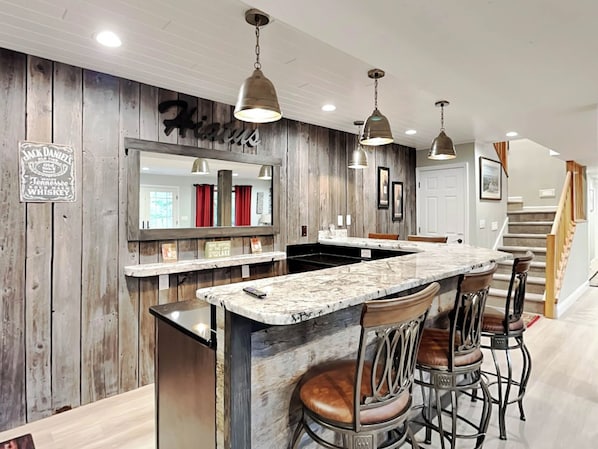A kitchen with a marble island, bar stools, pendant lights, and a wooden accent wall with a mirror and signs.