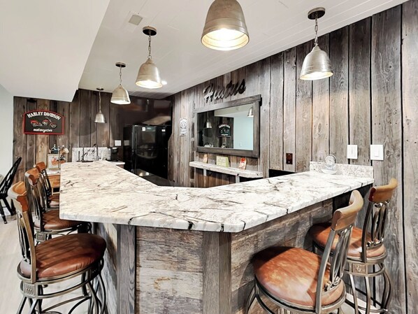 Una zona de bar con mostrador de mármol, taburetes de madera e iluminación colgante.