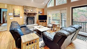 Una sala de estar acogedora con chimenea de piedra, sofás de cuero y televisión.