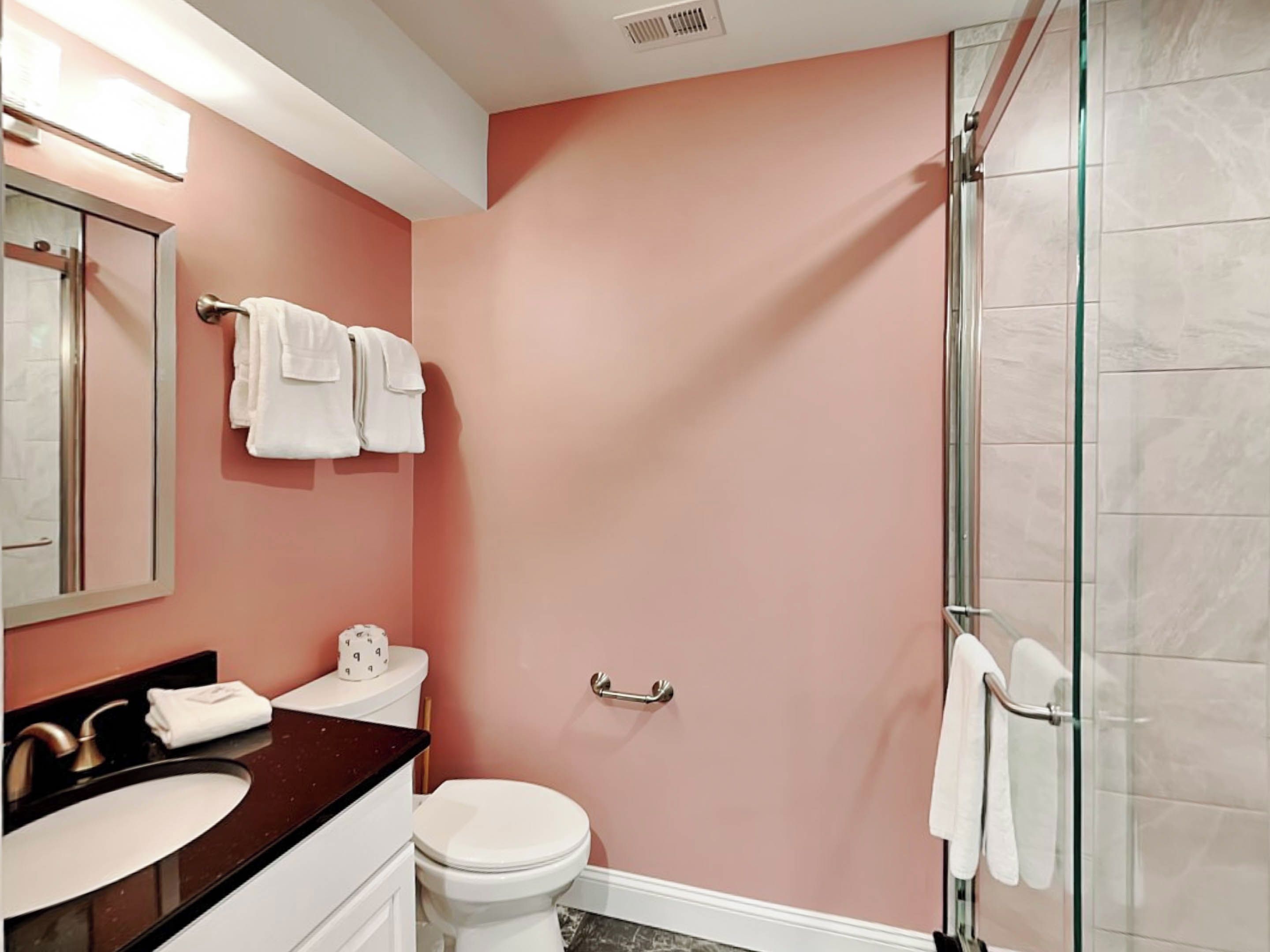 A bathroom with a pink wall, a white toilet, a black sink, and a glass shower enclosure.