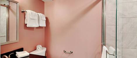 A bathroom with a pink wall, a white toilet, a black sink, and a glass shower enclosure.