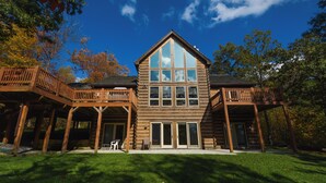 A large log cabin with a prominent central bay window, wooden balconies, and a covered patio area. - High-skis' Villa by Taylor Made Deep Creek (McHenry)
