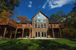 A large log cabin with a prominent central bay window, wooden balconies, and a covered patio area. - High-skis' Villa by Taylor Made Deep Creek (McHenry)