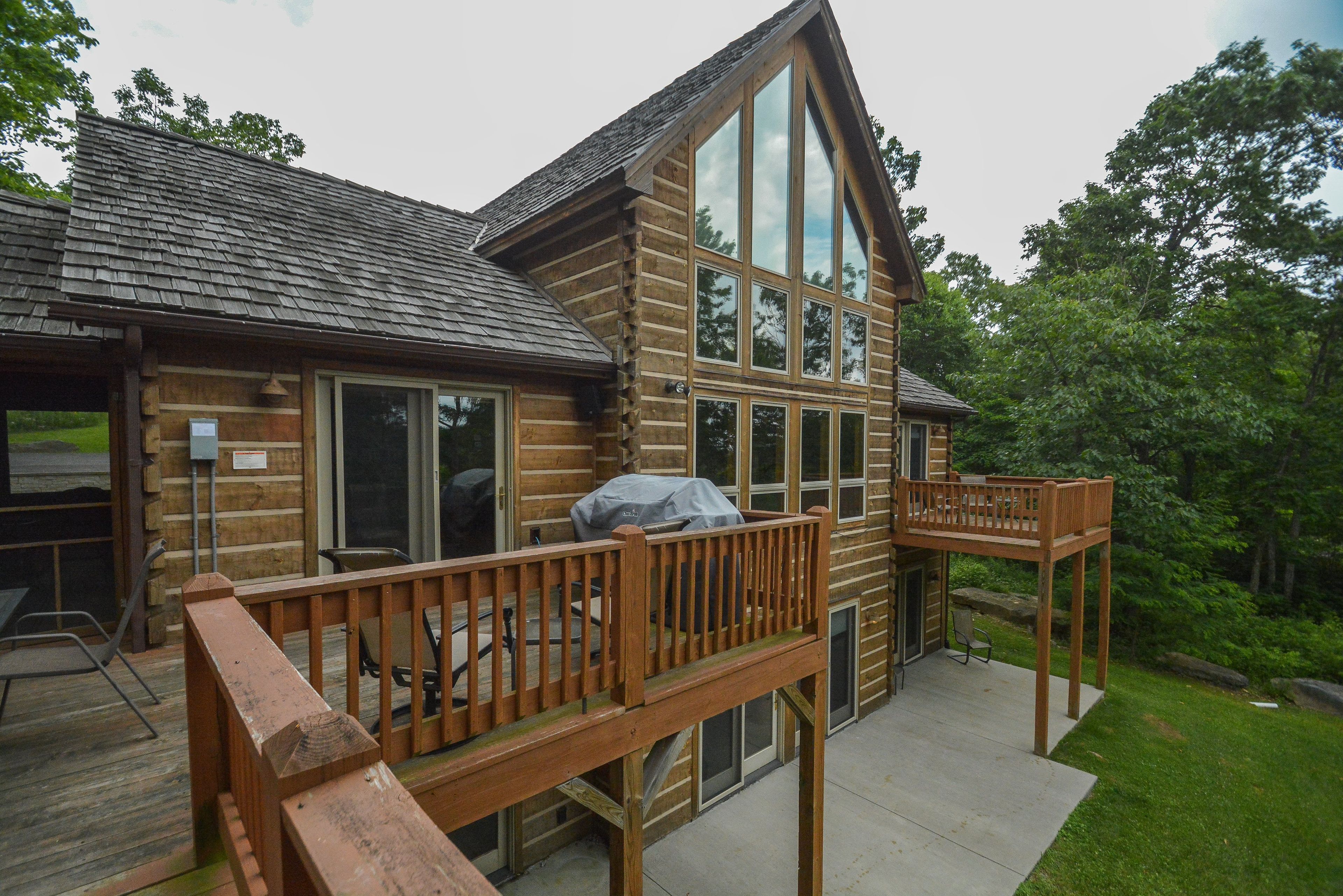 A log cabin with a deck, large windows, and a covered grill area.