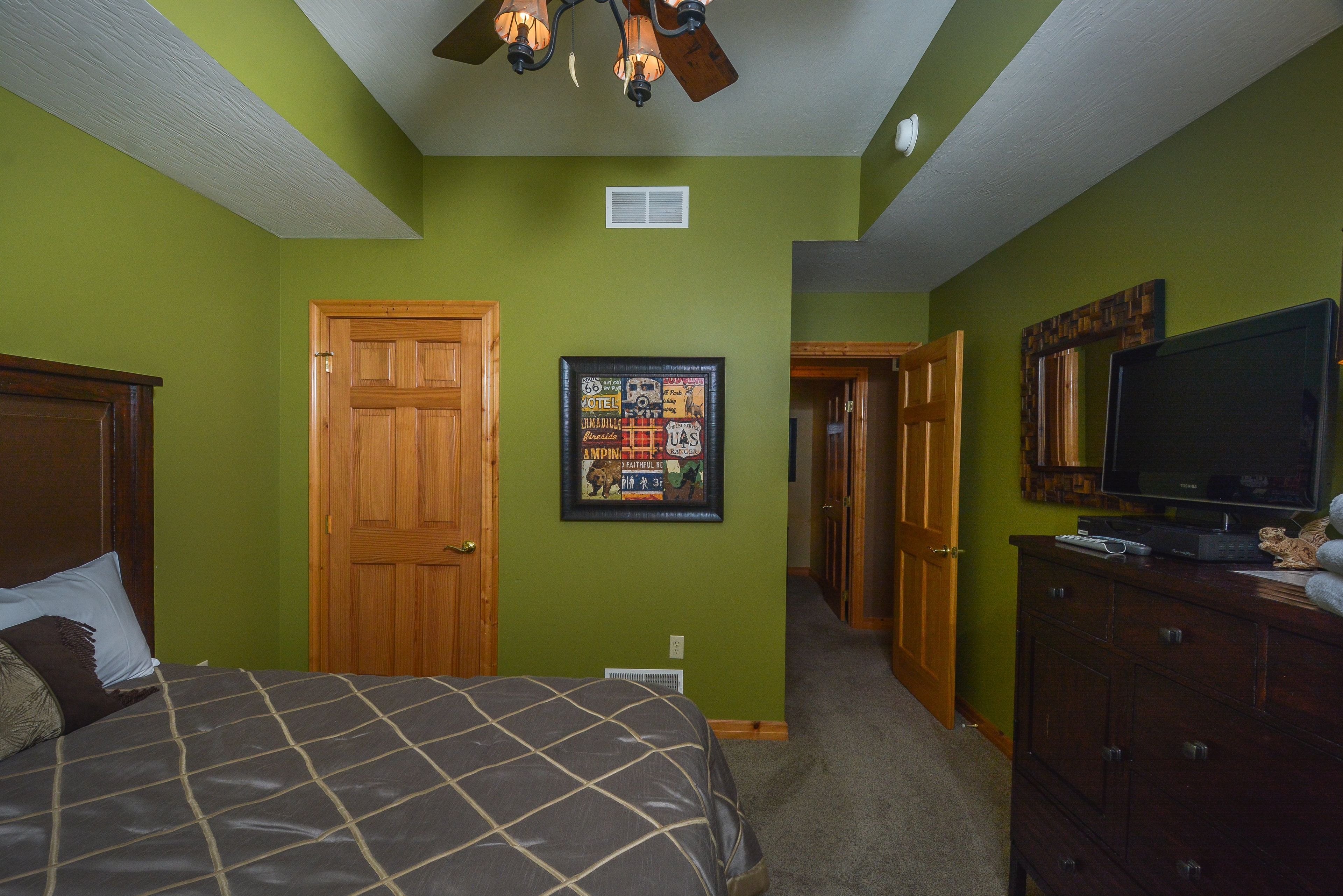 A bedroom with a bed, a wooden door, a framed picture on the wall, a dresser, and a television.