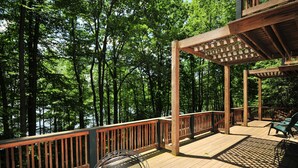 A wooden deck with a pergola, metal chairs, and a view of a forested area. - Highland Retreat by Taylor Made Deep Creek (McHenry)