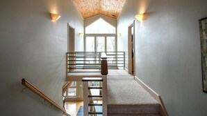 A staircase with a wooden handrail, carpeted steps, and a view of the outdoors through a large window. - Highland Retreat by Taylor Made Deep Creek (McHenry)