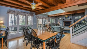 A dining area with a wooden table and chairs, a ceiling fan, and large windows with curtains. - Highland Retreat by Taylor Made Deep Creek (McHenry)