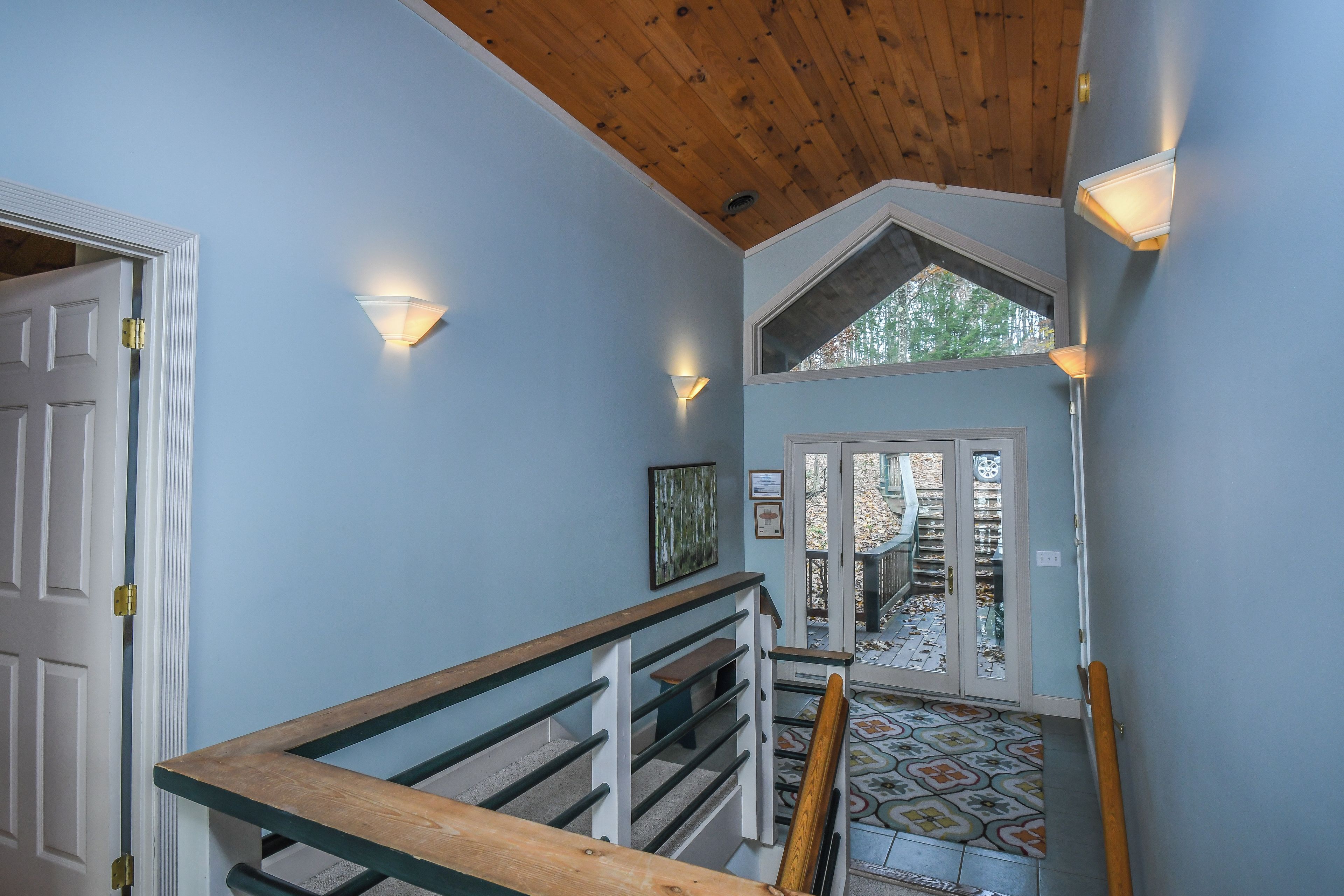A staircase with a wooden handrail, a white door, and a wall-mounted light fixture.