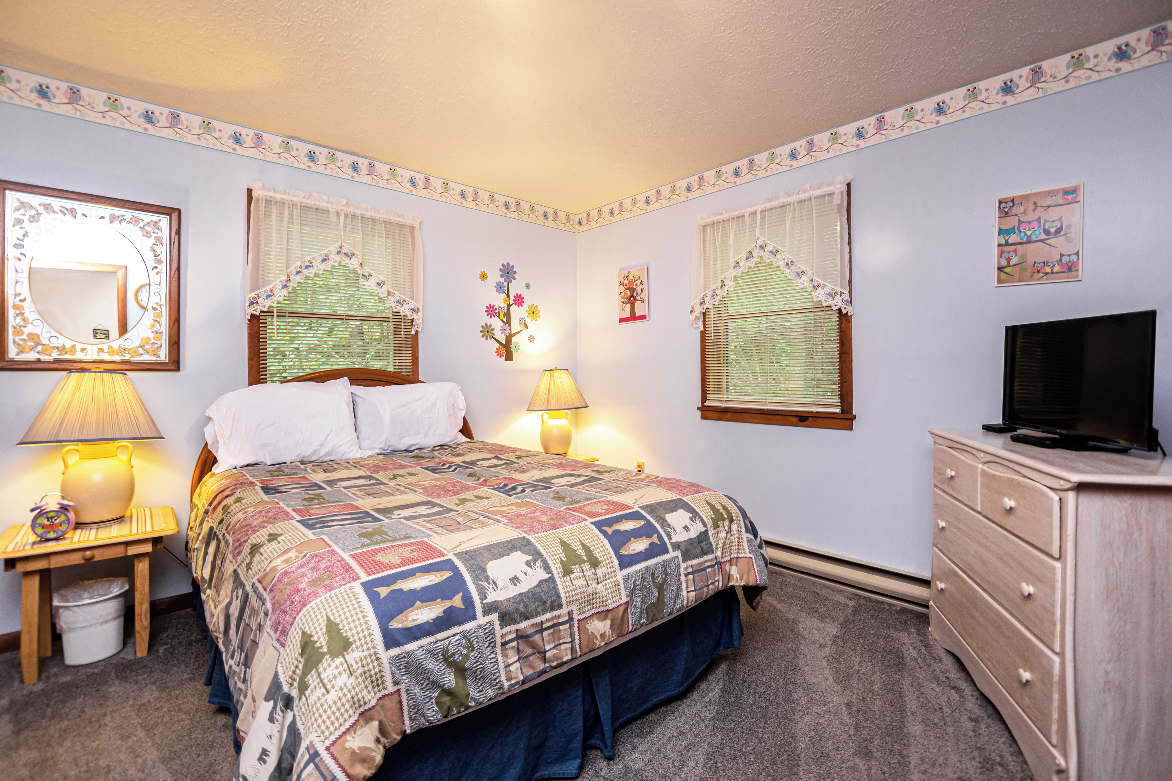 Une chambre à coucher comprenant un lit, des lampes de chevet, une commode, un téléviseur et des œuvres d’art décoratives accrochées au mur.