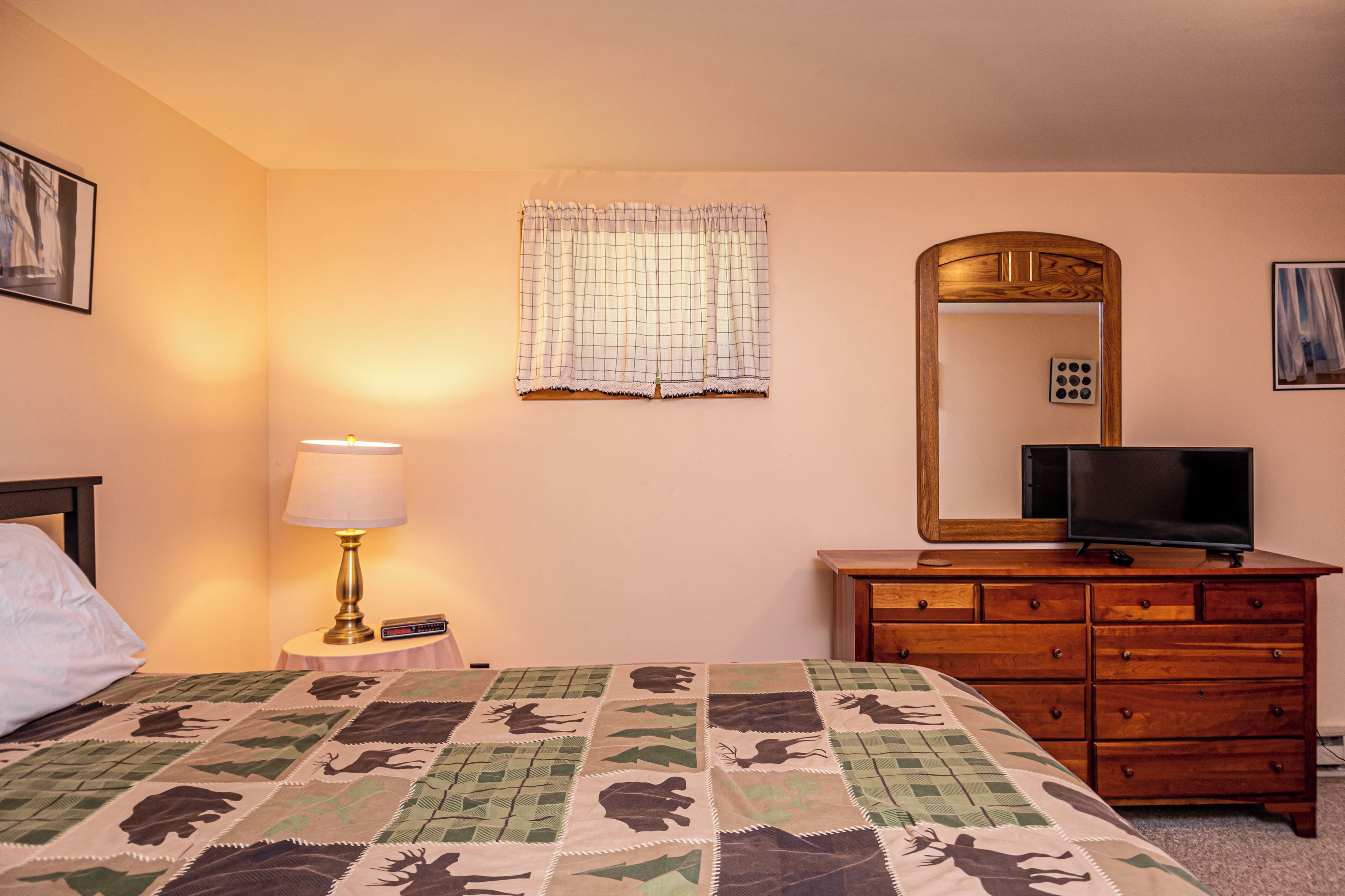 A hotel room with a bed, a dresser, a television, a lamp, a mirror, and a window with a curtain.