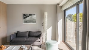 A modern living room with a grey sofa, a coffee table with pastries, a framed picture on the wall, and a large window with a view of the outside. - La Guimorais - La Maison du Benetin (Saint-Malo)