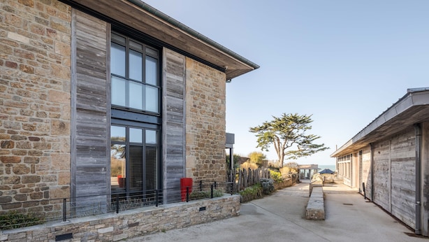 A modern building with stone walls and large windows, a concrete pathway, and a view of the ocean. - La Guimorais - La Maison du Benetin (Saint-Malo)