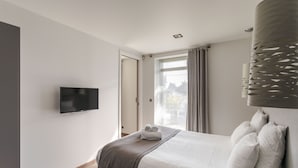 A modern hotel room with a large bed, a flat-screen TV mounted on the wall, and a window with curtains. - La Guimorais - La Maison du Benetin (Saint-Malo)