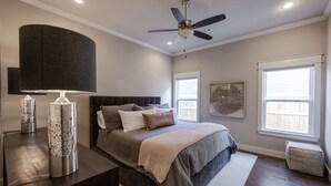 A bedroom with a bed, a ceiling fan, a window, and a nightstand with a lamp.