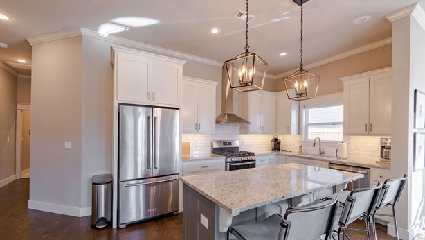 A modern kitchen with stainless steel appliances, a large island with bar stools, and pendant lighting.