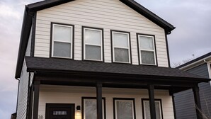A two-story house with a black front door, a covered porch, and a small front yard with a bench and potted plants.