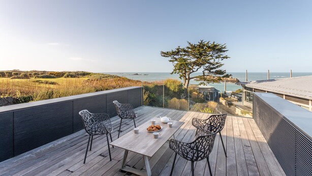 A wooden deck with a table and chairs overlooking a coastal landscape.