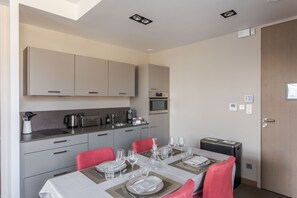 A modern kitchen with grey cabinets, a dining table set for four with red chairs, and a microwave above the counter. - Le Nicet - La Maison du Benetin (Saint-Malo)