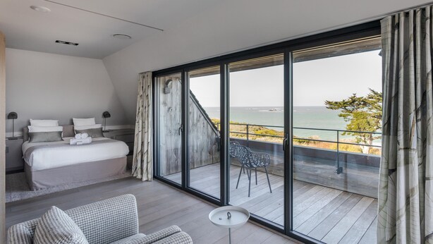 Un dormitorio con un amplio ventanal corredera que da a un balcón con vistas al mar.