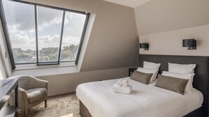 Un dormitorio moderno con un ventanal grande, una cama con ropa blanca, una silla y un escritorio.