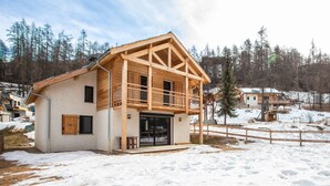 A wooden cabin with a balcony, a garage, and a snow-covered ground.