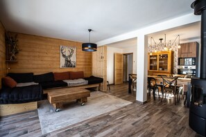 Uma sala moderna com piso de madeira, um sofá preto, uma mesa de centro de madeira e uma área de jantar com cadeiras de madeira e um lustre.