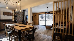 A spacious kitchen with a wooden dining table and chairs, a stone accent wall, and a large sliding glass door leading to a snowy outdoor area.