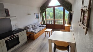Een gezellige kamer met kitchenette, een houten eettafel, een bank en een groot raam met uitzicht op de omgeving.