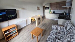Een knus woongedeelte met een houten tafel, een bank, een televisie en een boekenkast.
