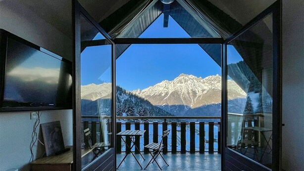 Een kamer met balkon en uitzicht op besneeuwde bergen.
