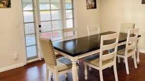 A dining area with a dark wooden table and white chairs, a glass door leading outside, and a small painting on the wall. - Cheerful home,4bedrooms,6beds,2baths,TV,Central AC (Fontana)