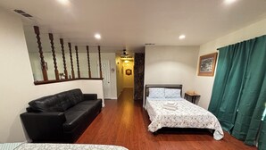 A hotel room with a wooden floor, a black leather sofa, two beds with floral bedding, a small bedside table, and a green curtain. - Cheerful home,4bedrooms,6beds,2baths,TV,Central AC (Fontana)