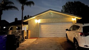 A residential garage with a white car parked inside, a garage door, and a number '9575' on the wall. - Cheerful home,4bedrooms,6beds,2baths,TV,Central AC (Fontana)