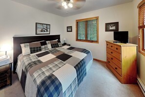 Une chambre à coucher comprenant un lit, une commode, un téléviseur et une fenêtre avec des stores.