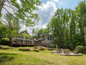 Een chalet met twee verdiepingen en een terras, omringd door een gazon en grote rotsen.