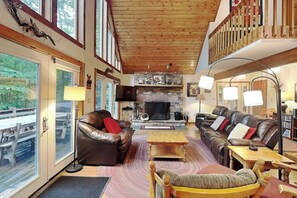 Un salón amplio con sofás de cuero, una chimenea y ventanas grandes con vistas a una terraza.