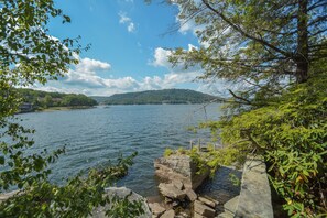 A lakeside view with a stone pier, lush greenery, and a distant hill. - Inspiration Point by Taylor Made Deep Creek (Swanton)
