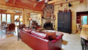 A cozy log cabin interior with a stone fireplace, wooden beams, and a red leather sofa. - Inspiration Point by Taylor Made Deep Creek (Swanton)