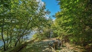 A stone pathway leading to a wooden bench area with a view of a lake and dense foliage. - Inspiration Point by Taylor Made Deep Creek (Swanton)