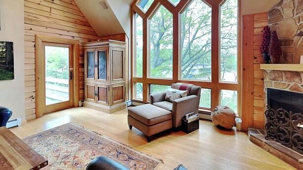 A spacious living room with a high ceiling, large windows, a stone fireplace, and a cozy seating area. - Inspiration Point by Taylor Made Deep Creek (Swanton)